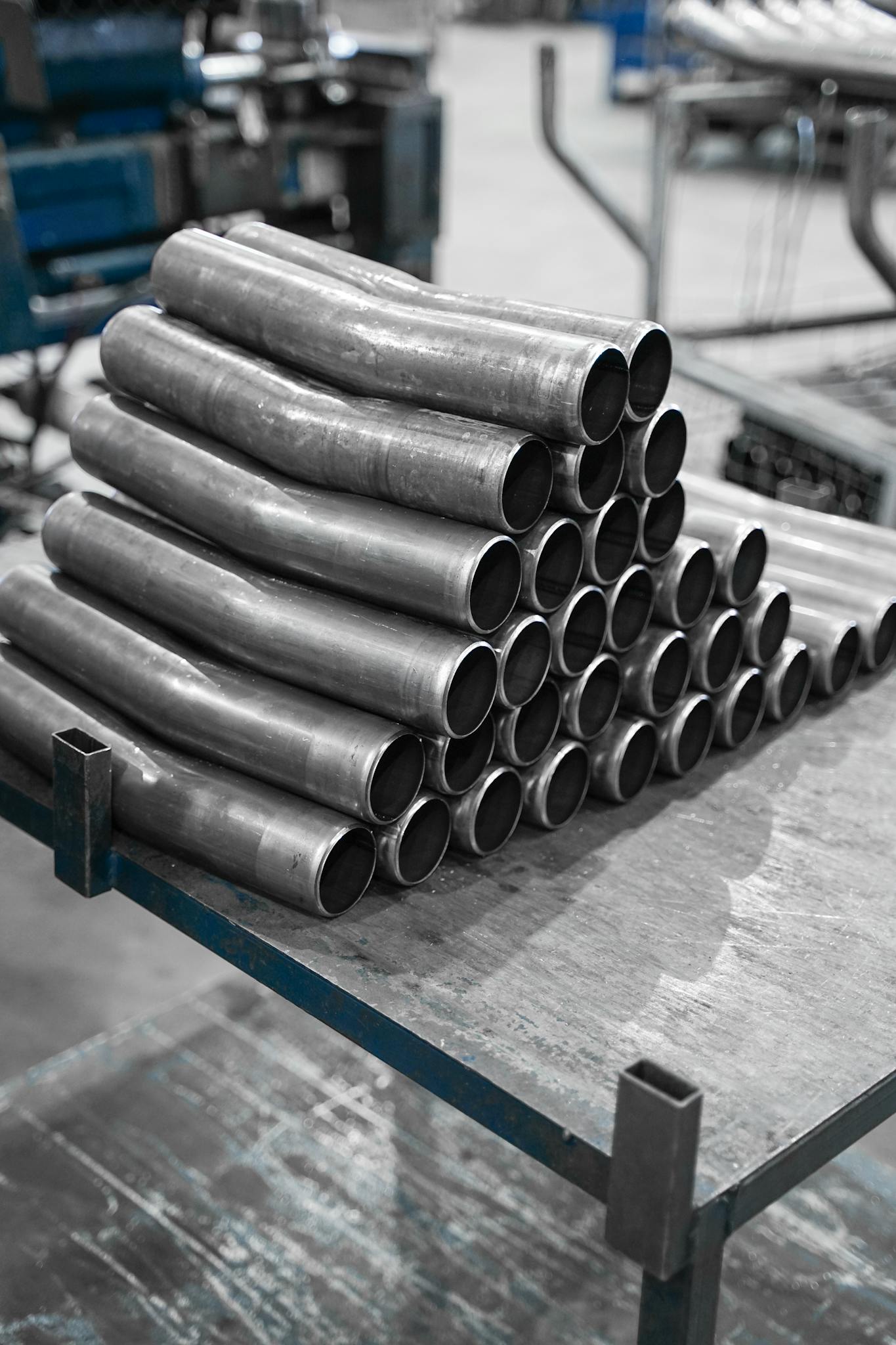 A stack of curved metal pipes displayed on a factory table in a manufacturing environment.